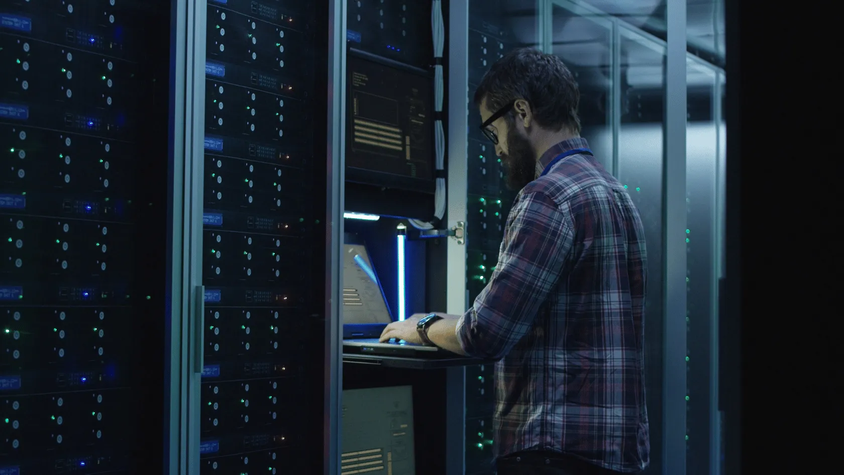 Technician working on a laptop inside a data center server aisle